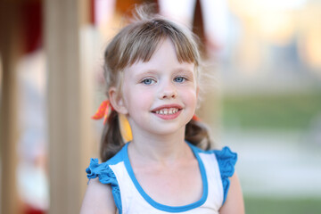 Portrait of little girl with blue eyes on background of playground. Outdoor walking for kids concept