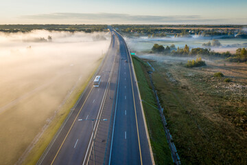 Straight road in the morning view from above. Transportation background. The bus is moving on the highway. Beautiful aerial landscape with road in colorful fog. Misty summer nature.