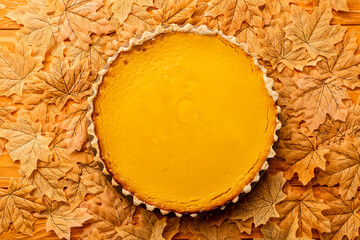 Wall Mural - top view of pumpkin pie with autumnal foliage on wooden background