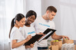 © LIGHTFIELD STUDIOS - Selective focus of multicultural volunteers looking at clipboards near paper bags in charity center