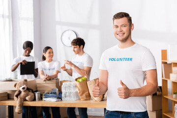 Selective focus of volunteer showing like gesture and looking at camera in charity center