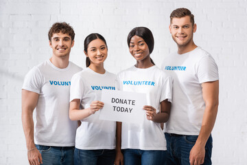 Multiethnic volunteers holding card with donate today lettering