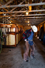 Male Rancher Putting On Chaps In Stable Barn