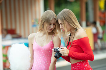 Two females friends having fun during outdoor photo session. Woman taking pictures. Blurred background.