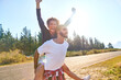 © Trevor Adeline/Caia Image - Portrait carefree young couple piggybacking at sunny remote roadside