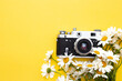 old camera and a bouquet of daisies on a yellow background