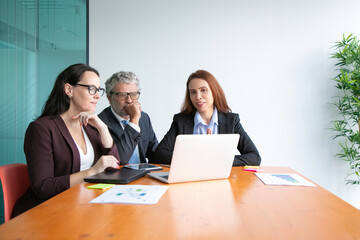 Group of professional watching presentation on computer, sitting at meeting table with charts in documents Medium shot. Marketing and teamwork concept