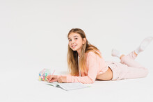 Cute Smiling Teen Girl With Long Hair In Pink Hoodie Doing Homework Isolated On The White Background