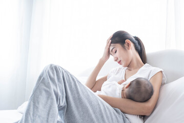 Mother breastfeeding her newborn baby beside window. Milk from mom’s breast is a natural medicine for children. Young woman feeding baby. The mother was exhausted from raising children.