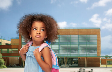 Wall Mural - childhood and education concept - sad little african american girl with backpack over school on background