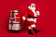 © deagreez - Ho-ho-ho. Full length photo of retired old man white beard hold sled giftbox walk snowy street wear santa x-mas costume coat sunglass headwear black boots isolated red color background
