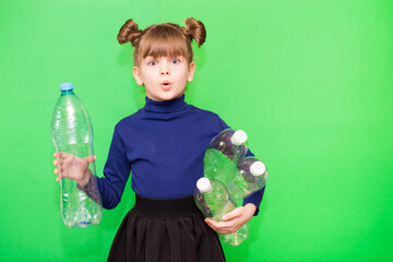 Photo of confused funny little girl holding plastic bottles and looking at camera isolated over green background