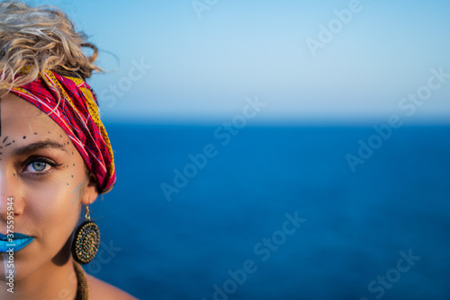 Plakat Half face portrait of a beautiful woman with ethnic African make up or face paint, and the blue sea on the background