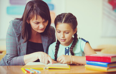 Wall Mural - Young beautiful teacher with schoolgirl reading book in the classroom