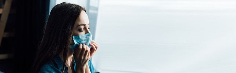 panoramic shot of brunette woman touching medical mask at home