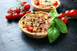Savory mini quiches or tarts on a rustic board. Flaky dough pies. Fresh basil and tomatoes on handmade quiche