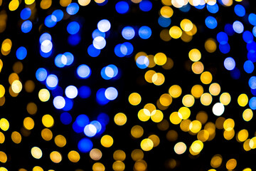 Blue and yellow colorful bokeh circles from New Year Christmas tree lights illuminations with defocused blurred view at night and black background
