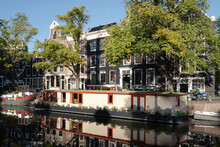 Houses And Houseboat Mirror In The Water Of The Prinsengracht Right Opposite The Anne Frank House In Amsterdam, Early In The Morning