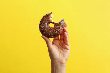 Wall Mural - Female hand hold tasty donut on yellow background