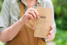 Woman Holds In Her Hands A Seed Bag With The Name Of The Flower Handwritten On It