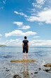 © Cara Dolan/Stocksy - Man stands on a rock at a beach, facing out to the ocean