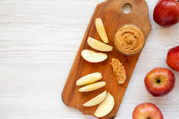 Wall Mural - Raw Red Apples and Peanut Butter on a rustic wooden board on a white wooden background, top view. Copy space.
