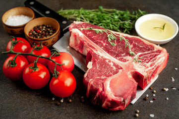 raw t-bone steak with ingredients on a meat knife on stone  background