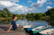 © FO_DE - A young man sits on a boat dock on a bright summer day.