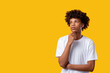 © golubovy - Create idea. Social tolerance. Pensive black teen boy with hand on chin isolated on orange copy space. Make decision. Disapproving emotion. Advertising background