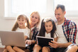 © Angelov - Happy family concept. Beautiful mother and handsome father with their daughters spending time together at home and lying on bed with laptop.