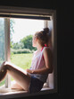 © Tana Teel Photography/Stocksy - Teenager sits in open window sill looking out