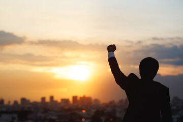 silhouette hand raised fist business man with sun lighting in morning. background city, success, grow up.