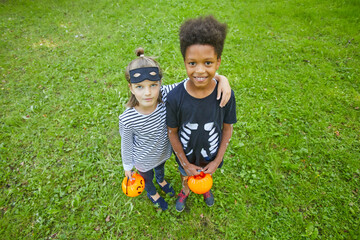 Portrait of two kids in Halloween costume embracing and smiling at camera while standing on the green grass outdoors