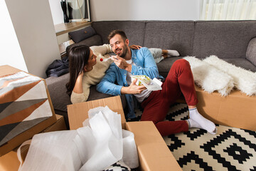 Wall Mural - Smiling young couple move into a new apartment, sitting in the living room eating and taking a break from unpacking.