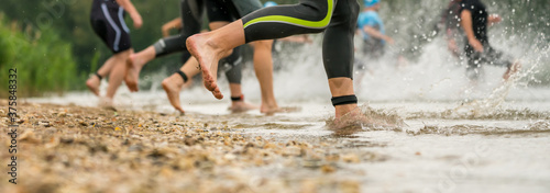Photographie Athletes in wetsuits running into a lake at a triathlon competition