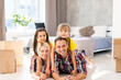 © Angelov - Caucasian family, man, woman and two girls sit on floor, unpack boxes and smile in new house. Behind them moving boxes.