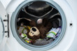 Kleiner brauner Teddybär mit Schmutzwäsche in einer Waschmaschine. Hygiene, Desinfektion, Nahaufnahme.