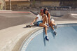 © puhhha - Portrait Of Skater Girls At Skatepark. Female Teenagers In Casual Outfit Sitting On Concrete Ramp. Summer Skateboarding With Modern Sport Equipment As Part Of Active Lifestyle.