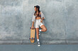 © puhhha - Skater Girl At Skatepark. Full-Length Portrait Of Female Hipster In Casual Outfit With Skateboard Against Concrete Wall At Skate Park. Urban Subculture Style And Summer Sport In City. Active Lifestyle