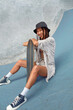 © puhhha - Skateboarding. Asian Girl In Urban Outfit With Skateboard Sitting On Ramp Against Concrete Wall At Skatepark. City Sport As Hobby For Active Teens. Skater Subculture And Summer Activity As Lifestyle.