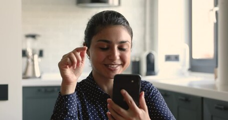 Indian ethnicity business woman freelancer sit at home studio apartments holding mobile phone modern wireless device. Woman looks at screen talking with colleague friend or client using video