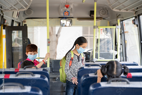Cuadros en Lienzo Kids with medical mask coming inside school bus and sitting on seats while maint