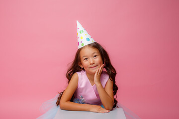 Wall Mural - a little girl of Asian appearance with a cap on her head celebrates her birthday on a pink background