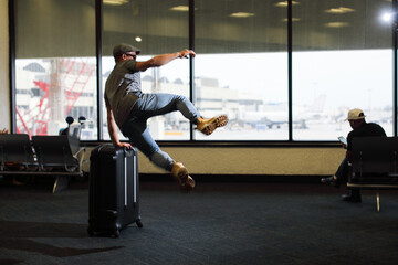 man jumping near the suitcase in airport and looking through the window on aircraft 
