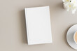 White book mockup with a cup of coffee and oleander on a beige table.