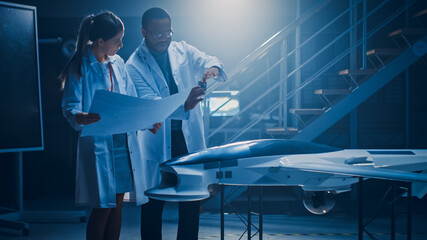Poster - Two Aerospace Engineers Work On Unmanned Aerial Vehicle / Drone Prototype. Aviation Scientists in White Coats Holding Blueprints. Laboratory with Commercial Aerial Surveillance Aircraft