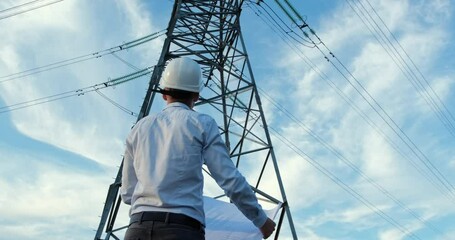 Wall Mural - a man in a white protective helmet stands facing a high-voltage power line pole with a paper drawing