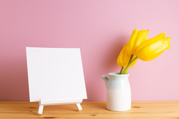 Wall Mural - Blank canvas on easel with yellow tulip flowers on wooden table with pink background