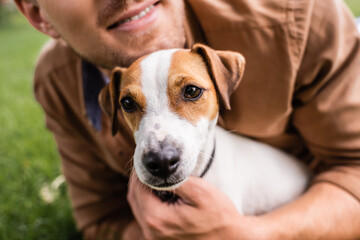 Cropped view of man cuddling jack russell terrier dog while lying on green grass