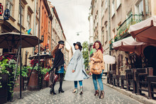 Stylish Women Walking On City Street. Three Girlfriends Having Fun In Lviv Outdoors. Autumn Fashion
